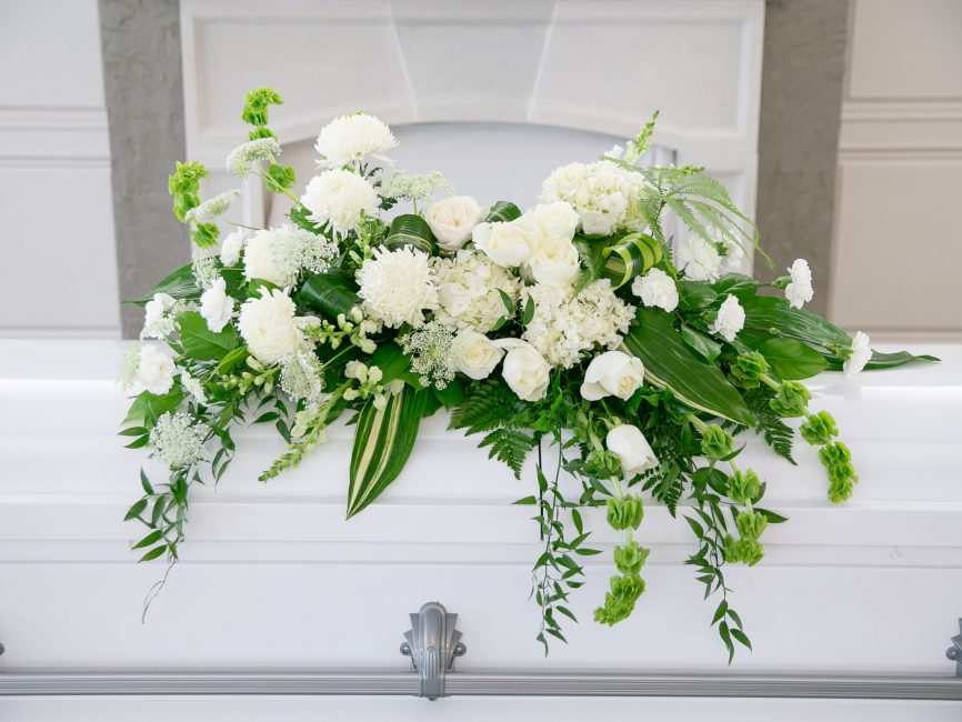 Dignity casket spray with white blooms and greenery by Studley Flower Gardens